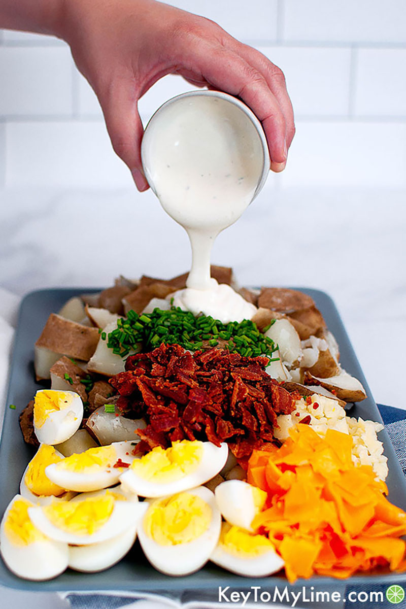 Hand-Pouring-Sauce-Baked-Potato-Egg-Salad