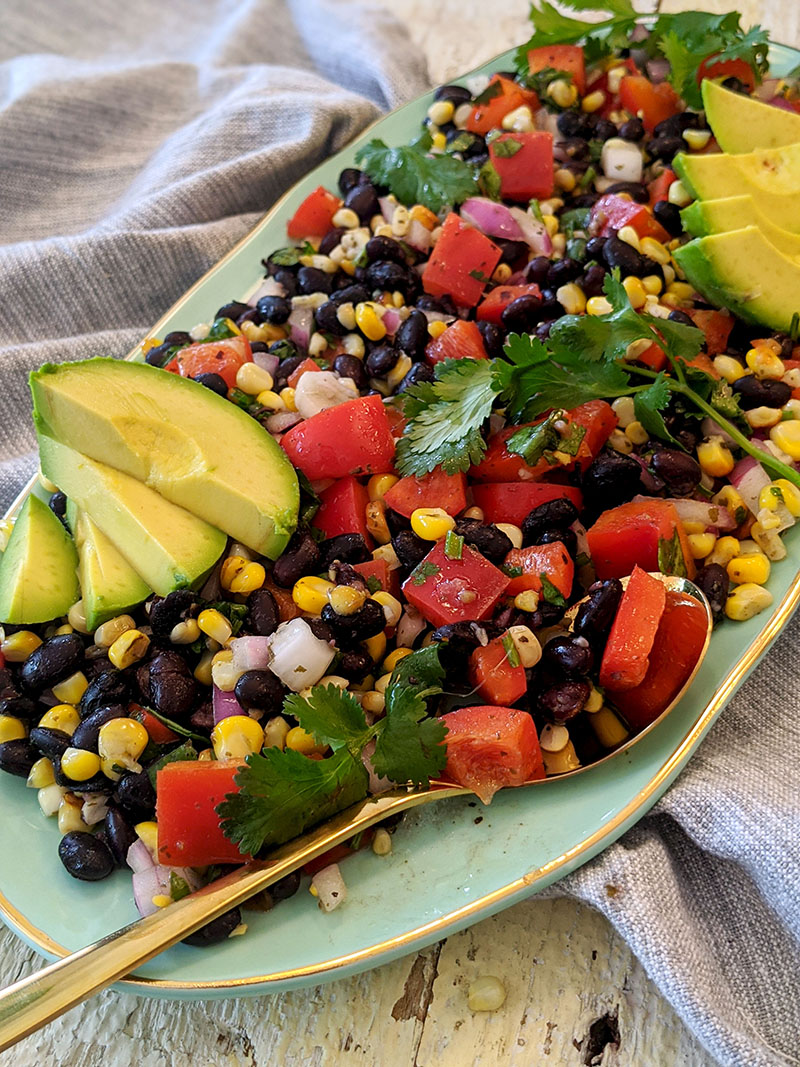 Charred corn salad with cilantro dressing and sliced avocado on a serving platter