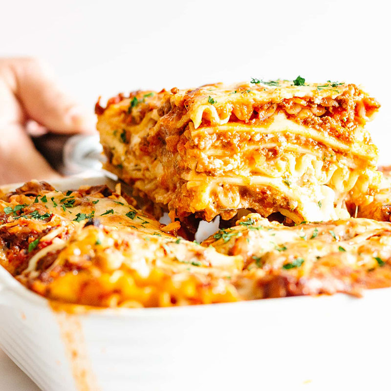 A slice of lasagna being removed from a baking dish