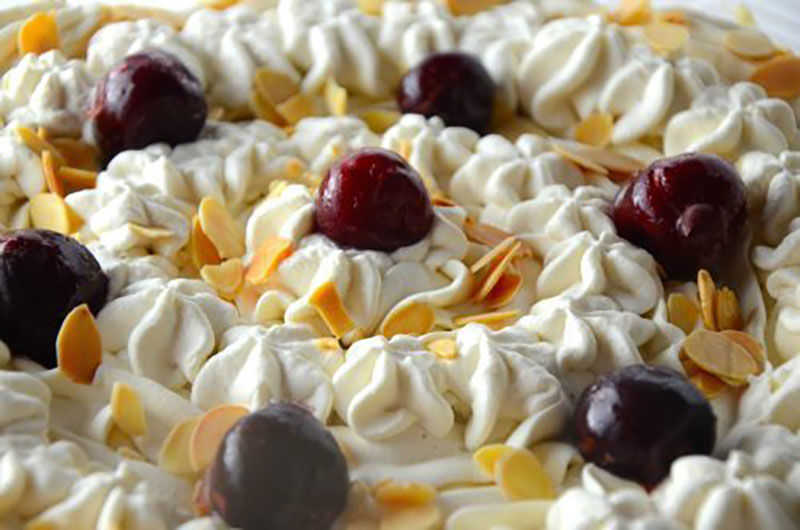 the top of a trifle covered with whip cream and cherries