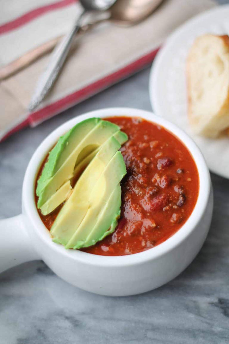 a bowl of beef chili topped with sliced avocado