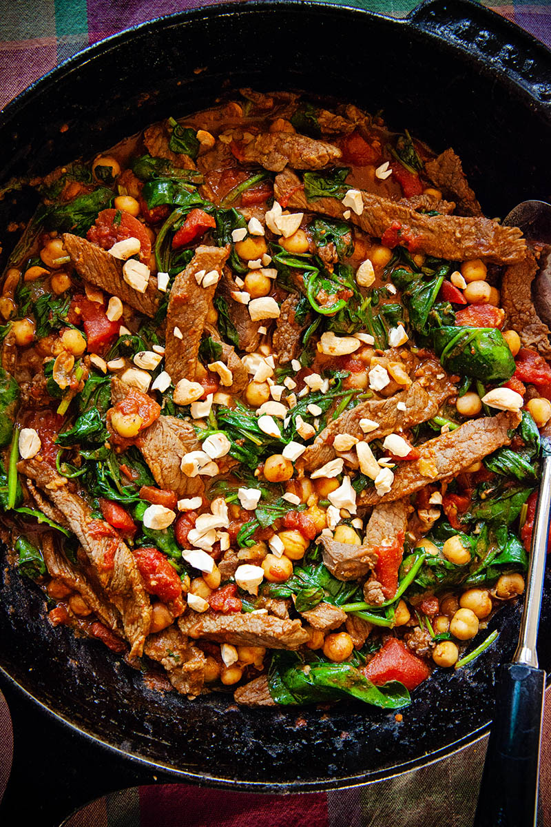 A skillet full of colourful chickpea beef curry with spinach and tomatoes
