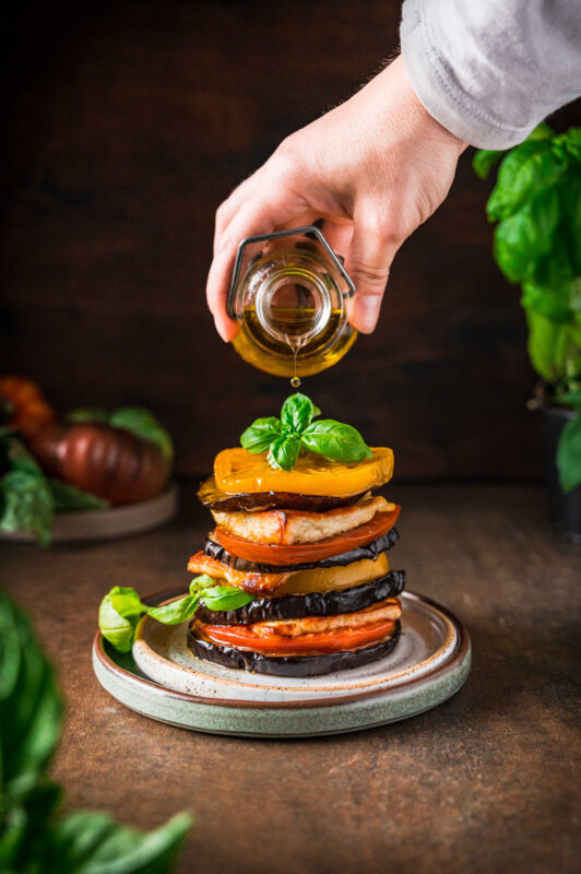 Eggplants on a plate, hand above with jar.