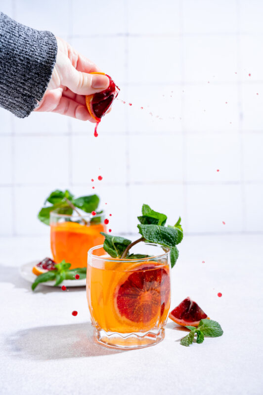 Drink with bloody orange, hand above the drink.